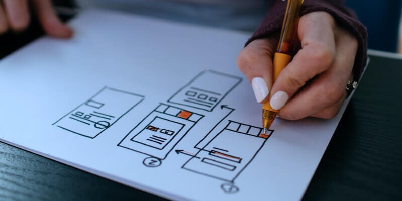 lady-hand-with-white-painted-nails-colouring-buttons-on-ui-design-sketch-on-white-paper